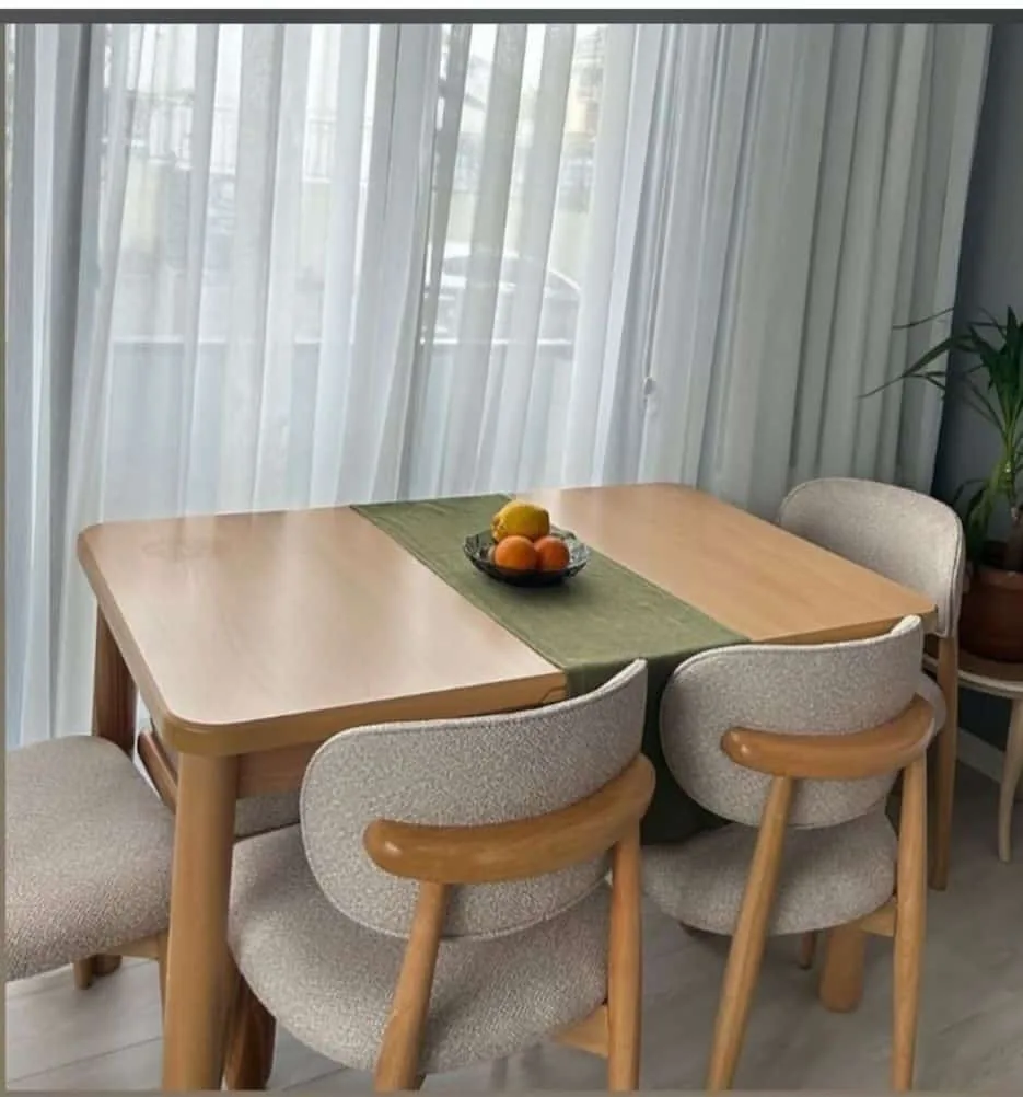 Pencere önünde meşe renk açılır masa ve dört krem bukle kollu sandalye