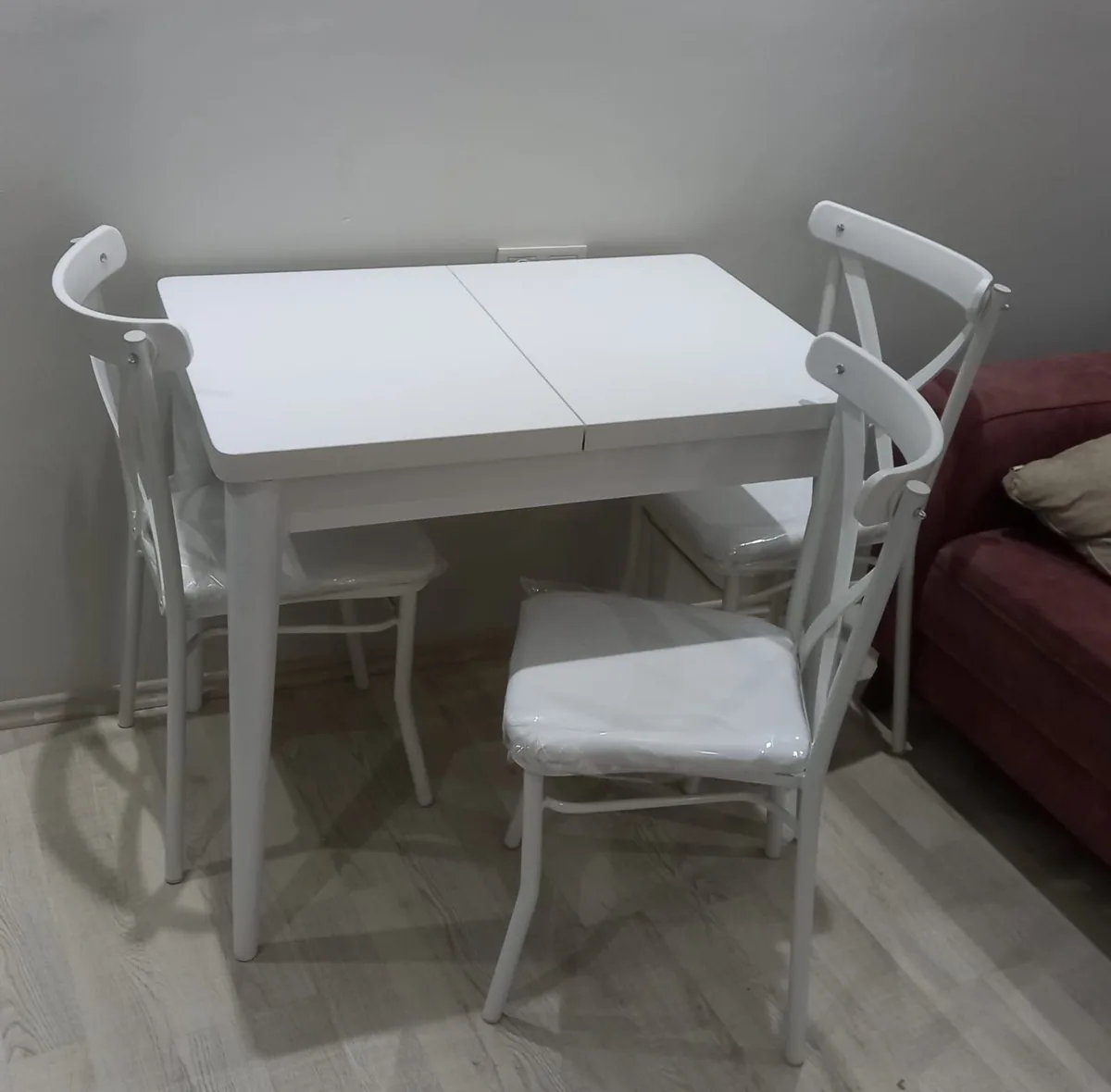 Beyaz açılır mutfak masası ve dört beyaz çapraz sırtlı sandalye